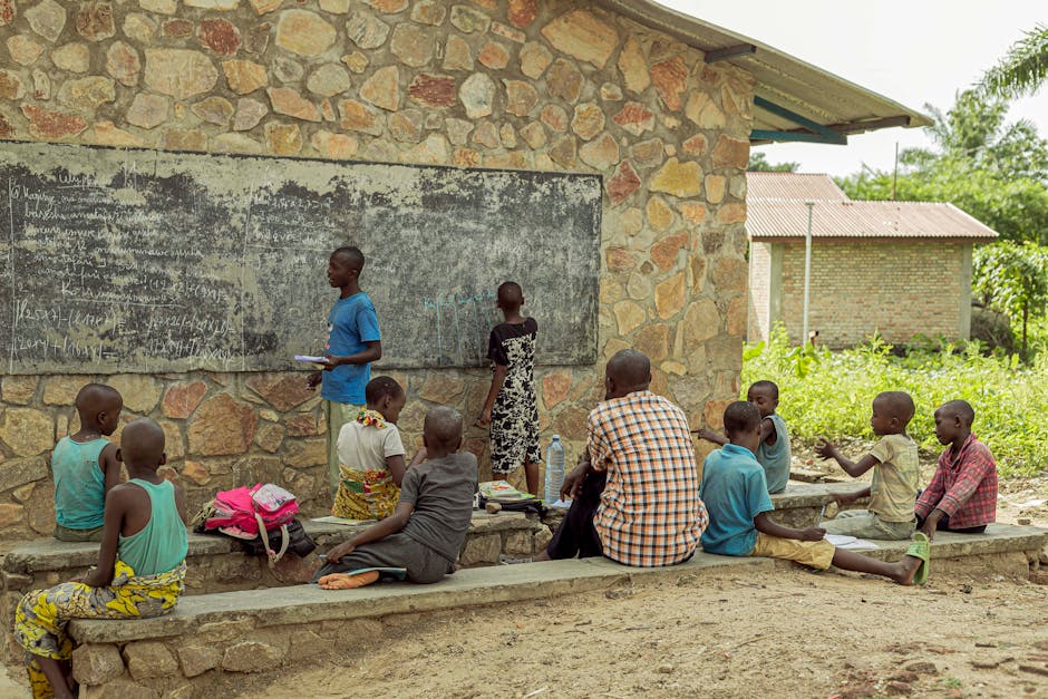 Children learning in an outdoor classroom setting with a chalkboard and stone wall backdrop